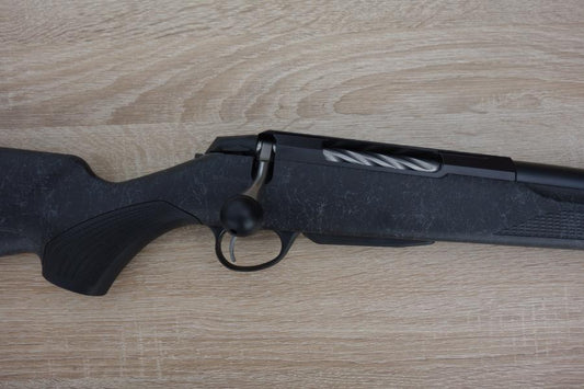 Tikka T3X Roughtech rifle with a fluted barrel, detachable magazine, and oversized bolt handle, displayed on a wooden surface.
