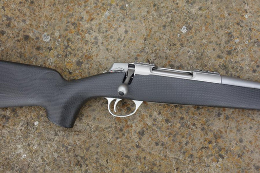 Sako 90 Peak Carbon rifle with carbon fibre stock, fluted barrel, adjustable trigger, and detachable magazine, showcased on a textured surface.