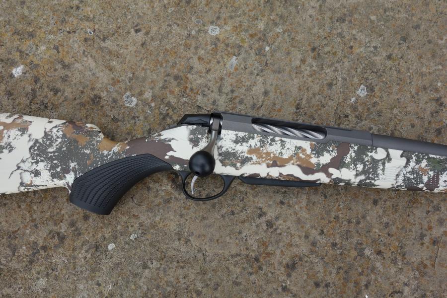 Close-up of Tikka T3X Camo FLS rifle, showcasing the fluted barrel and oversized bolt handle, with a Cerakoted receiver and factory muzzle brake.