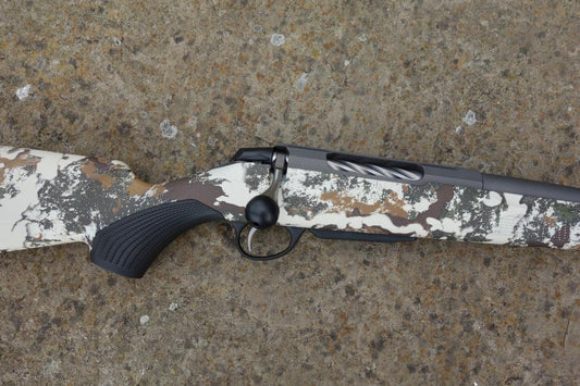 Close-up of Tikka T3X Camo FLS rifle, showcasing the fluted barrel and oversized bolt handle, with a Cerakoted receiver and factory muzzle brake.