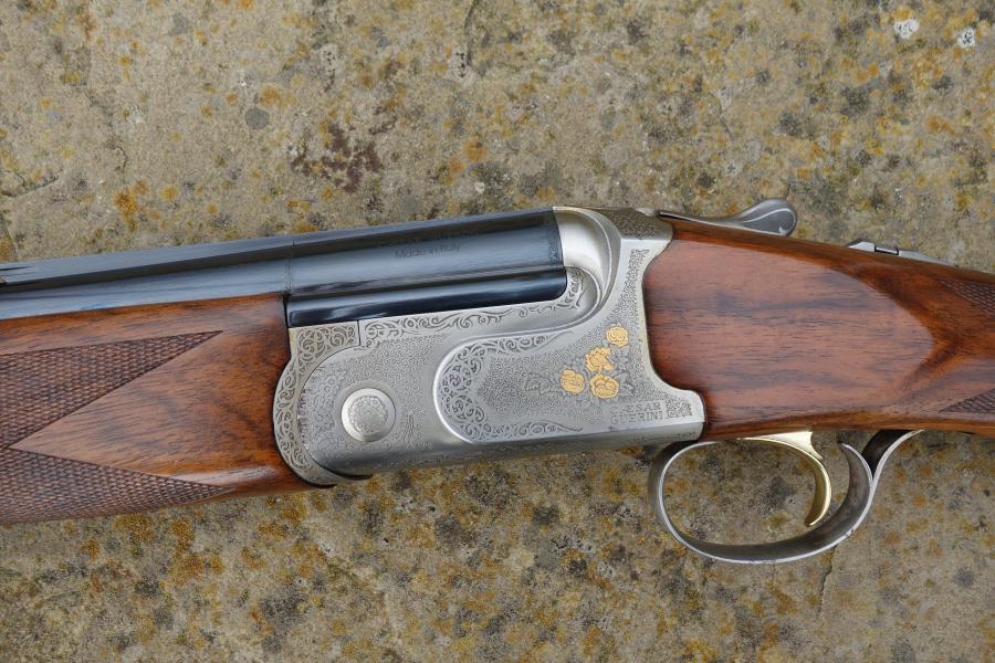 Caesar Guerini Tempio Game shotgun on stone surface, showcasing detailed engravings, rounded pistol grip, and visible trigger, emphasizing its superb condition and craftsmanship.