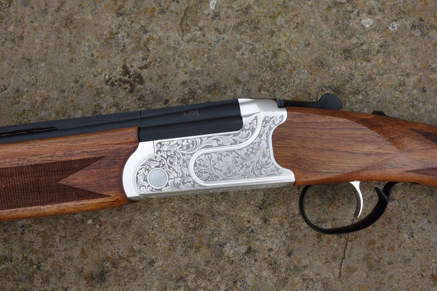 Kofs Sceptre SXE Game shotgun with silver-black handle, visible trigger, and finely figured stock, featuring HP steel proofed barrel and auto safety catch.