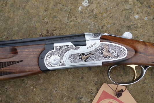 Close-up of the ATA Elegant Gold Game gun, showcasing its handle and trigger, with a brown tag attached. Features include multi chokes and automatic safety catch.