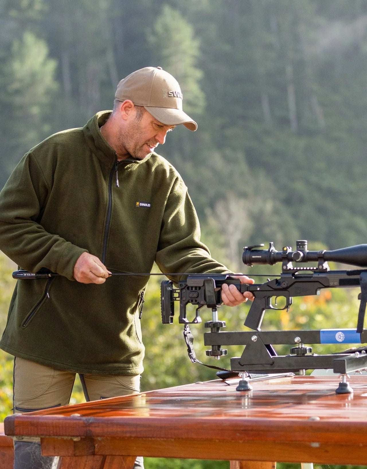 Man wearing Swazi Doughroaster Fleece Jumper, holding a rifle outdoors. Jumper features high collar, long chest zip, and kangaroo pocket for functionality.