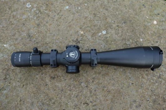 Leupold MK 5HD 5-25x56 Rifle Scope on concrete; features TMR reticule, zero stop turret, side parallax, includes aluminium lens cover, and picatinny rings.