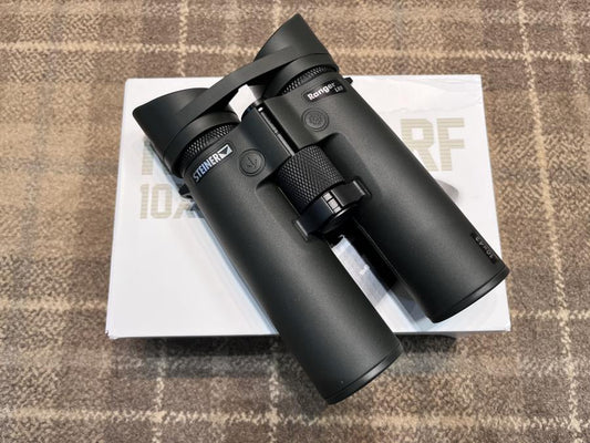 Steiner Ranger LRF 10x42 Binoculars atop a white box, featuring integrated laser range finder and inclinometer for precise distance measurement.