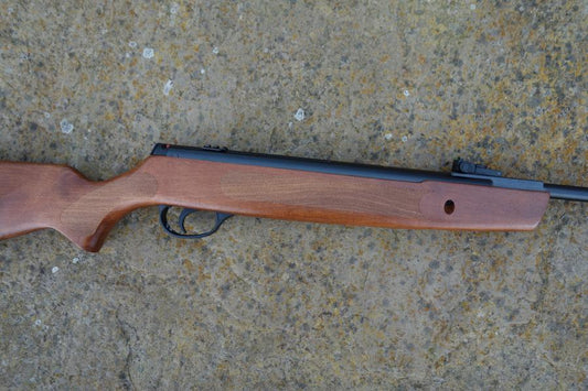 Hatsan Striker 1000S lies on the ground, showcasing its beech stock and Hi-viz open sights, ideal for mounting scopes and shooting sports.