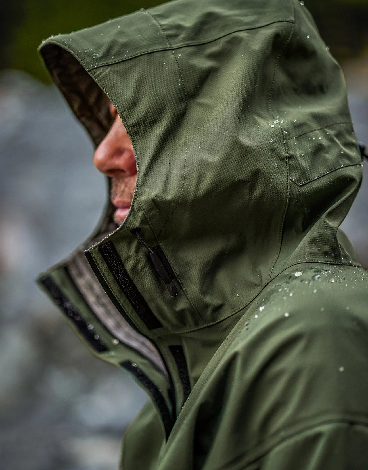 Swazi Tahr Ultralite Jacket showcasing its green waterproof, windproof design with a full-length zipper, visible high periphery vision hood, and adjustable features for outdoor use.