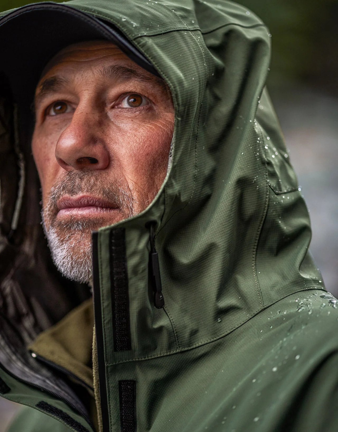 Man wearing Swazi Tahr Ultralite Jacket, featuring a high-vision hood and chest pockets, ideal for waterproof and breathable hunting or hiking in windy conditions.