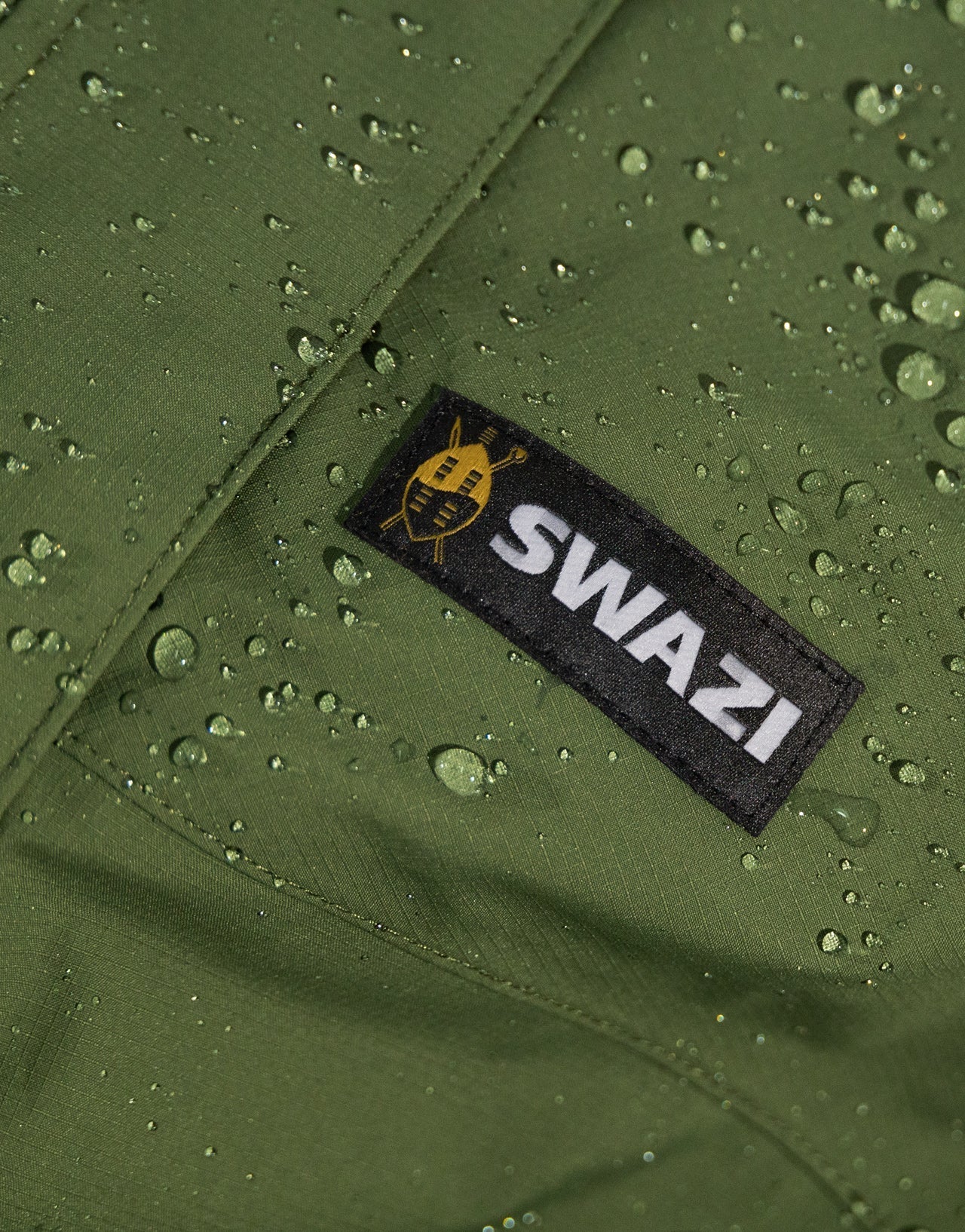 Swazi Tahr Ultralite Jacket with visible water droplets, showcasing its waterproof nature. Features include a high-vision hood and zippered chest pockets.