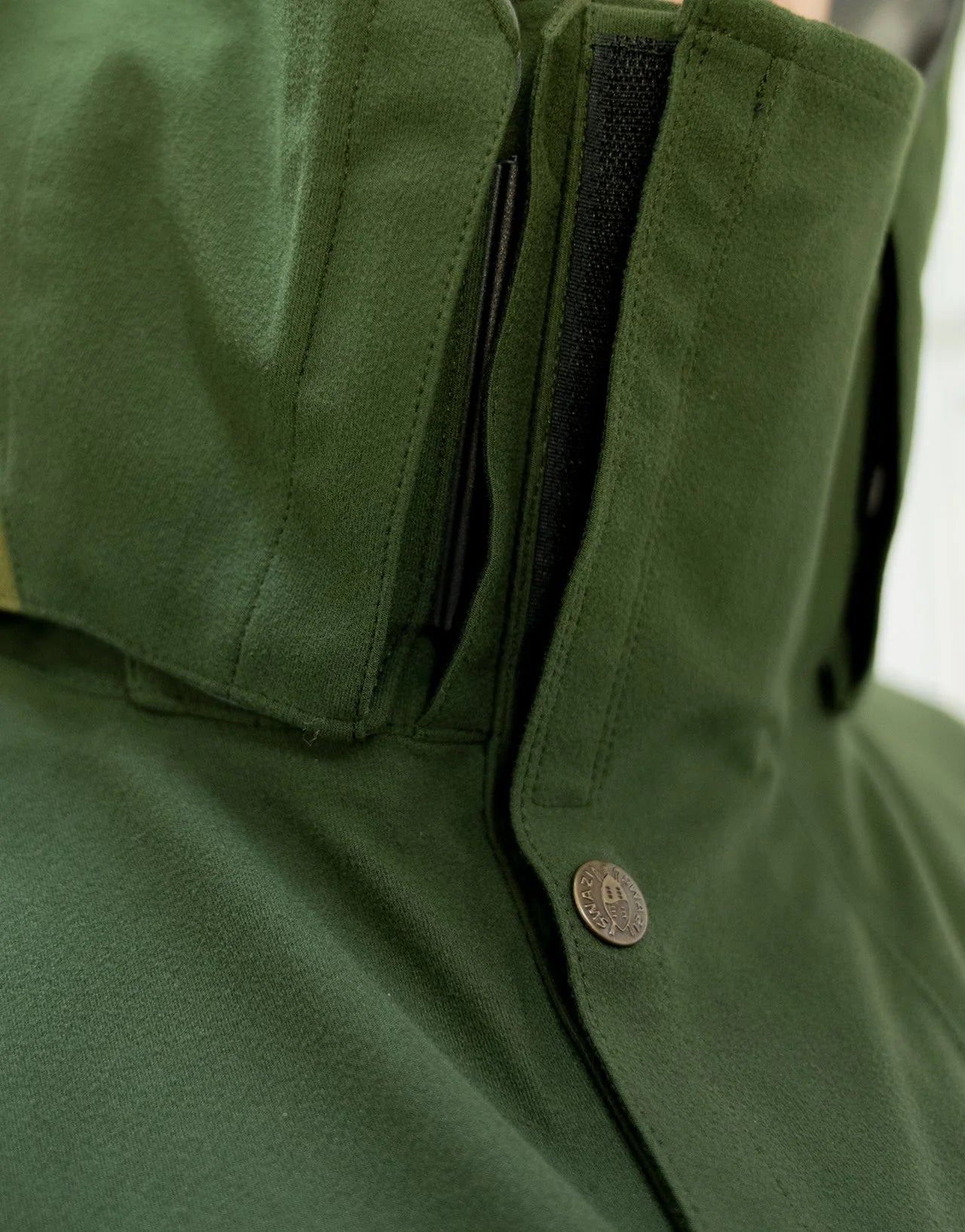 Swazi Wapiti XP Men's Hunting Jacket with a close-up of zipper, green waterproof fabric, zip-off hood, and accessible pockets designed for rugged outdoor conditions.