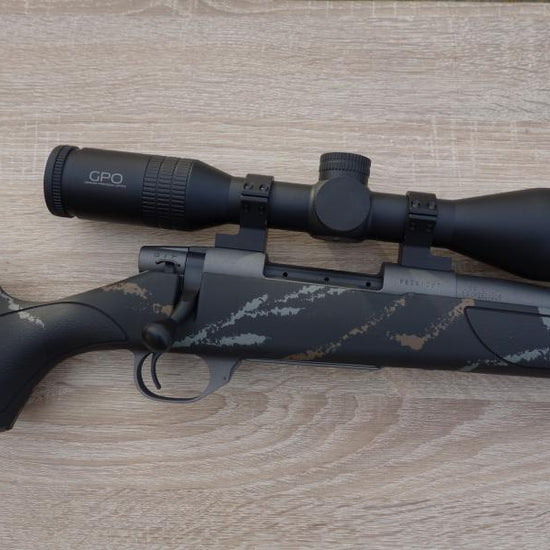 Weatherby Meateater rifle on a table, featuring a GPO 7x50 scope, bi-pod, and spiral fluted barrel, showcasing its precision design and included accessories.