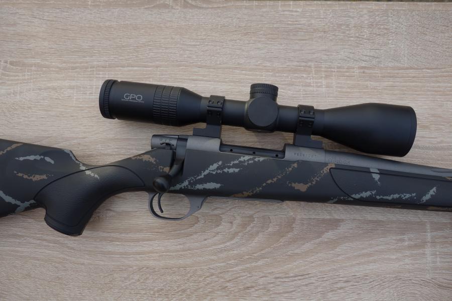 Weatherby Meateater rifle on a table, featuring a GPO 7x50 scope, bi-pod, and spiral fluted barrel, showcasing its precision design and included accessories.