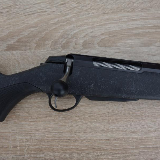 Tikka T3X Roughtech rifle with a fluted barrel, detachable magazine, and oversized bolt handle, displayed on a wooden surface.