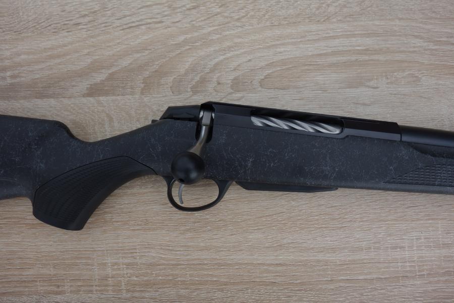 Tikka T3X Roughtech rifle with a fluted barrel, detachable magazine, and oversized bolt handle, displayed on a wooden surface.