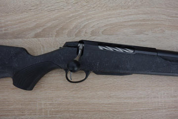 Tikka T3X Roughtech rifle with a fluted barrel, detachable magazine, and oversized bolt handle, displayed on a wooden surface.