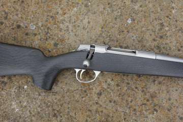 Sako 90 Peak Carbon rifle with carbon fibre stock, fluted barrel, adjustable trigger, and detachable magazine, showcased on a textured surface.