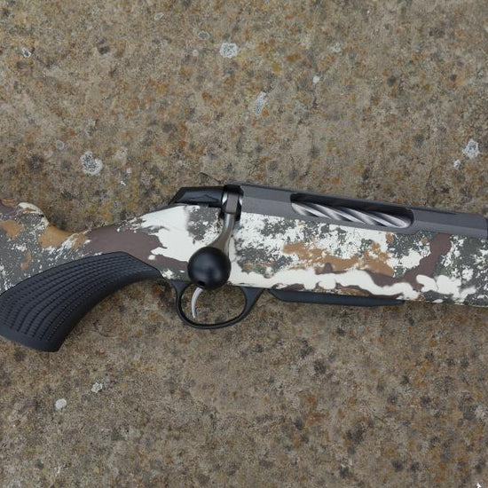 Close-up of Tikka T3X Camo FLS rifle, showcasing the fluted barrel and oversized bolt handle, with a Cerakoted receiver and factory muzzle brake.