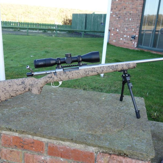 Howa 1500 HS Precision rifle on a stand, featuring a scope, Picatinny rail, and bi-pod, highlighting its precision optics and durable construction.