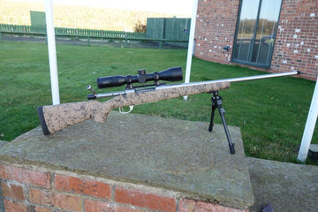 Howa 1500 HS Precision rifle on a stand, featuring a scope, Picatinny rail, and bi-pod, highlighting its precision optics and durable construction.