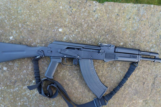Izmash M3 EXP-01 rifle, featuring a straight pull design, strap, folding butt, and adjustable sights, placed on a stone surface.