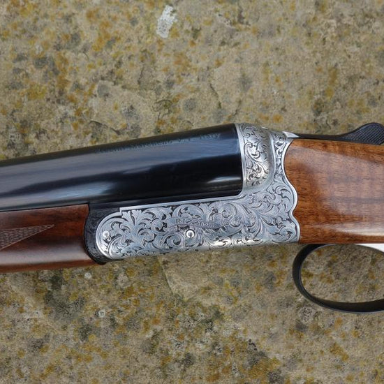 Rizzini BR550 Side by Side featuring elegant scroll engraving, walnut stock with pistol grip, visible trigger, and gun barrel details.