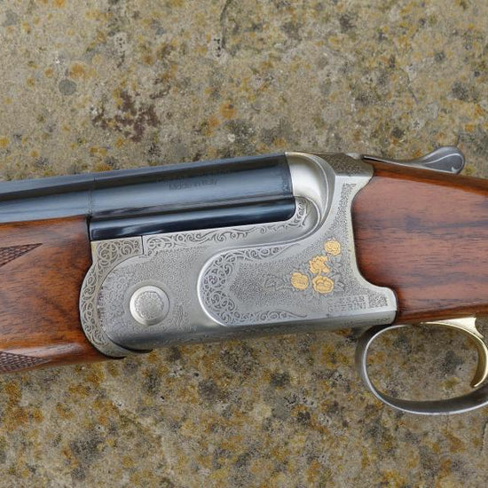 Caesar Guerini Tempio Game shotgun on stone surface, showcasing detailed engravings, rounded pistol grip, and visible trigger, emphasizing its superb condition and craftsmanship.