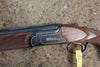 B Rizzini BR240 Sporting gun with gold accents, walnut stock, and pistol grip, featuring vent rib barrels and multi chokes, shown on the ground.