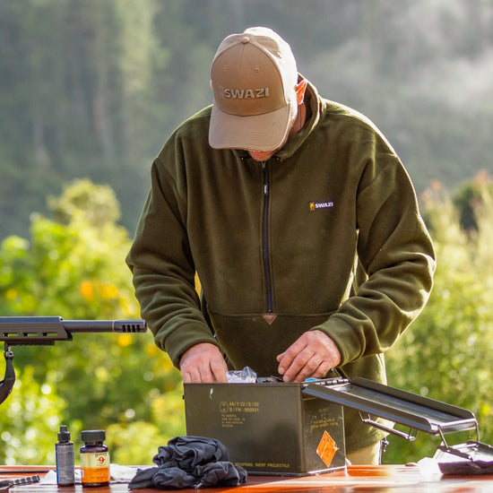 Man wearing Swazi Doughroaster Fleece Jumper, adjusting box. Features a long zip, high collar, large pocket, and adjustable hem. Ideal for comfort and versatile use.