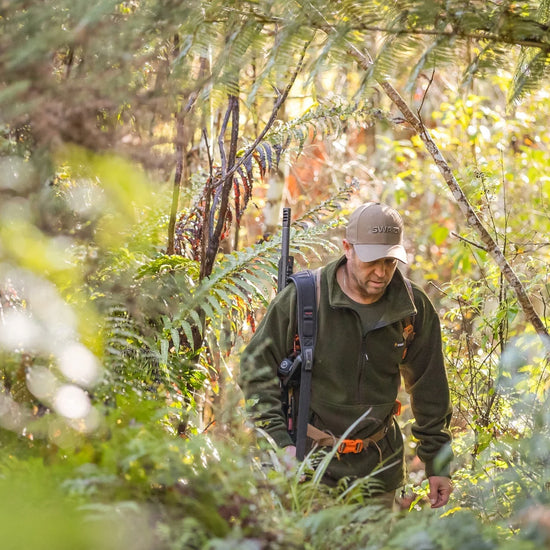 Swazi Doughroaster Fleece Jumper in use: Man walking in woods, wearing a hat, green jacket, and backpack, highlighting its outdoor functionality and comfort.