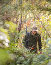 Swazi Doughroaster Fleece Jumper in use: Man walking in woods, wearing a hat, green jacket, and backpack, highlighting its outdoor functionality and comfort.
