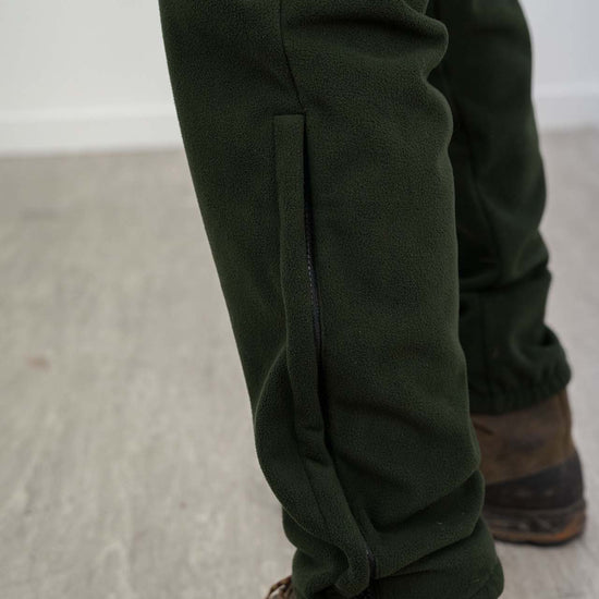 Person wearing Swazi 4WD Pants, windproof fleece trousers, featuring deep pockets and zipper cuffs over boots, designed for comfort and warmth during outdoor activities.