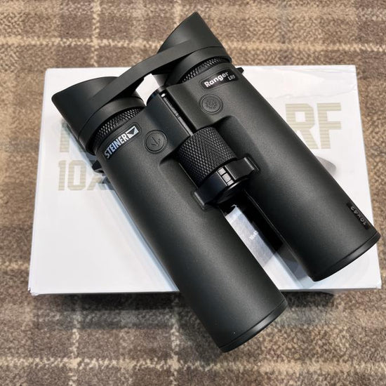 Steiner Ranger LRF 10x42 Binoculars atop a white box, featuring integrated laser range finder and inclinometer for precise distance measurement.