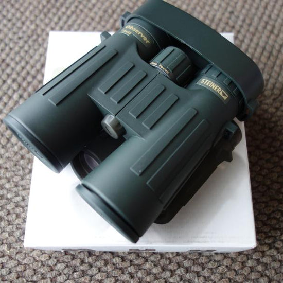Steiner Observer 8X42 Binoculars resting on a white box, showcasing their ergonomic design and compact build for outdoor enthusiasts.