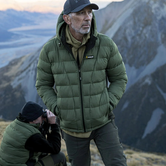 Swazi Puffadder Men's Puffer Jacket with detachable hood, shown on a mountaineer standing outdoors, highlighting its tailored fit and practical features for cold conditions.