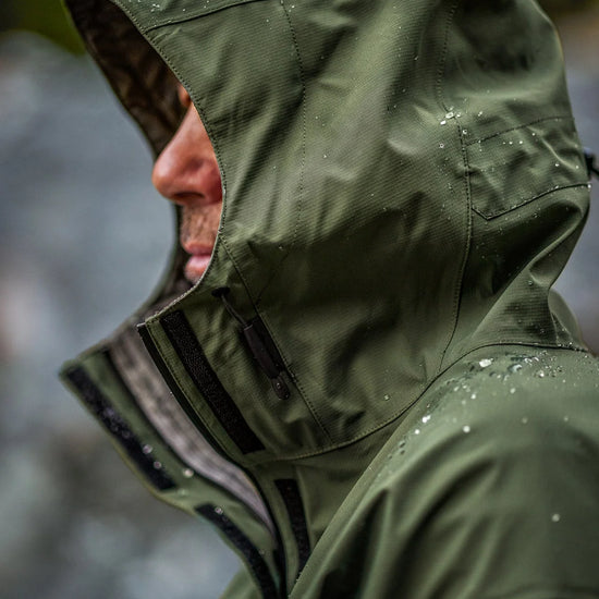 Swazi Tahr Ultralite Jacket showcasing its green waterproof, windproof design with a full-length zipper, visible high periphery vision hood, and adjustable features for outdoor use.
