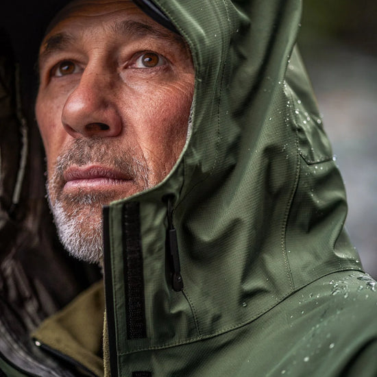Man wearing Swazi Tahr Ultralite Jacket, featuring a high-vision hood and chest pockets, ideal for waterproof and breathable hunting or hiking in windy conditions.