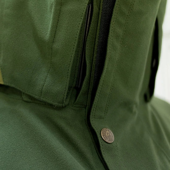 Swazi Wapiti XP Men's Hunting Jacket with a close-up of zipper, green waterproof fabric, zip-off hood, and accessible pockets designed for rugged outdoor conditions.